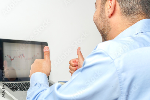 Businessman reacting with euphoria to the positive results he sees on his laptop graph by placing his thumbs up as a sign that everything is going very well.