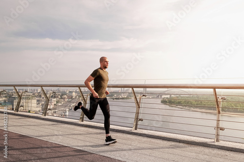 Fotografiet Young European man runs on the pedestrian bridge in the city at dawn