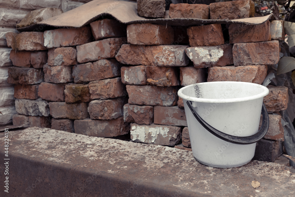 White plastic bucket next to a pile of old bricks. Old dirty bucket