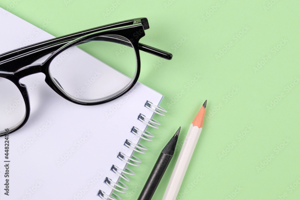 A spring-loaded notebook,white and black pencils,stylish glasses on a delicate green background.Things for businessmen, schoolchildren,students,teachers, artists, education, top view.Copyspace A spring-loaded notebook,white and black pencils,stylish glasses on a delicate green background.Things for businessmen, schoolchildren,students,teachers, artists, education, top view.Copyspace