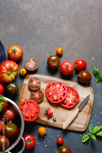 Fresh colorful ripe fall or summer heirloom variety tomatoes with knife and chopping board over wooden table background. Harvest and cooking tomato sauce concept