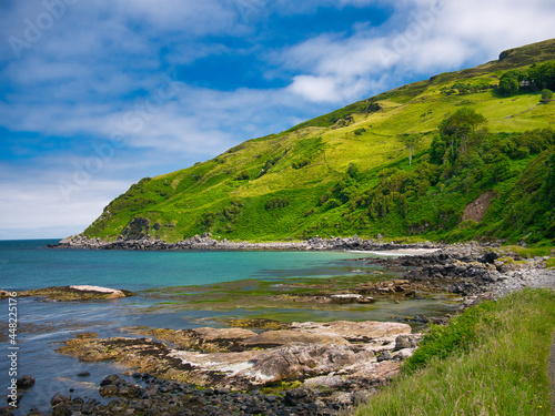 The clear blue water and green hills around Murlough Bay on the spectacular Antrim Causeway Coast in Northern Ireland, UK - taken on a calm, sunny day in summer with blue sky and blue water.