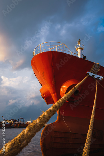 Konstfotografi Low angle view of cargo ship docked at port against rain cloudy sky at sunset ti