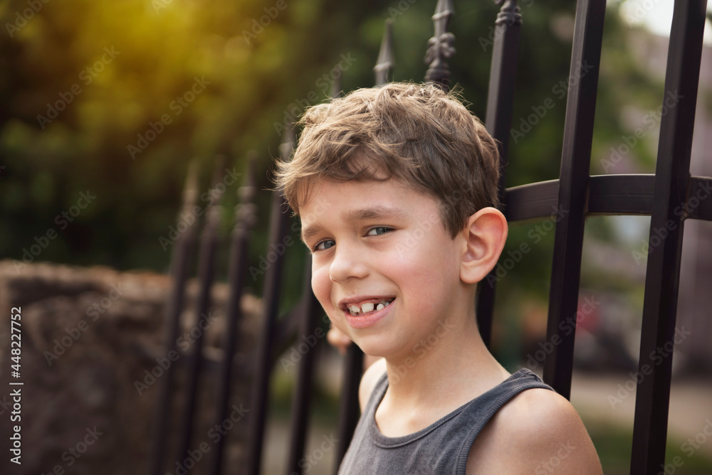 Obraz premium The little boy rests in the shade after a long walk during the hot summer weather, the boy smiles and shows his healthy permanent teeth that grow to replace the already bad baby teeth