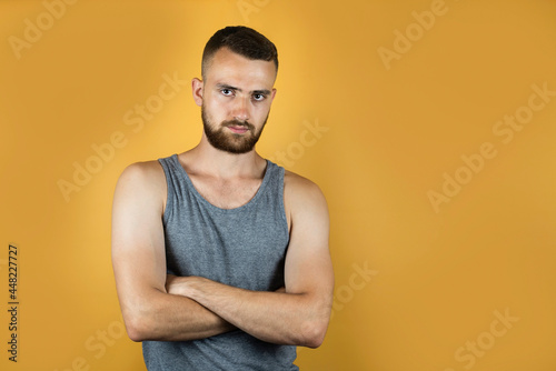 Portrait of a young man in a gray T-shirt on a yellow background, thanks to the beard the guy looks older, more serious and he likes it