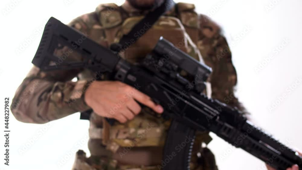 Soldier in modern military outfit and body armor with an assault rifle in his hands enters the frame from defocus. White background. Isolated. Soldier in modern military outfit and body armor with an assault rifle in his hands enters the frame from defocus. White background. Isolated.