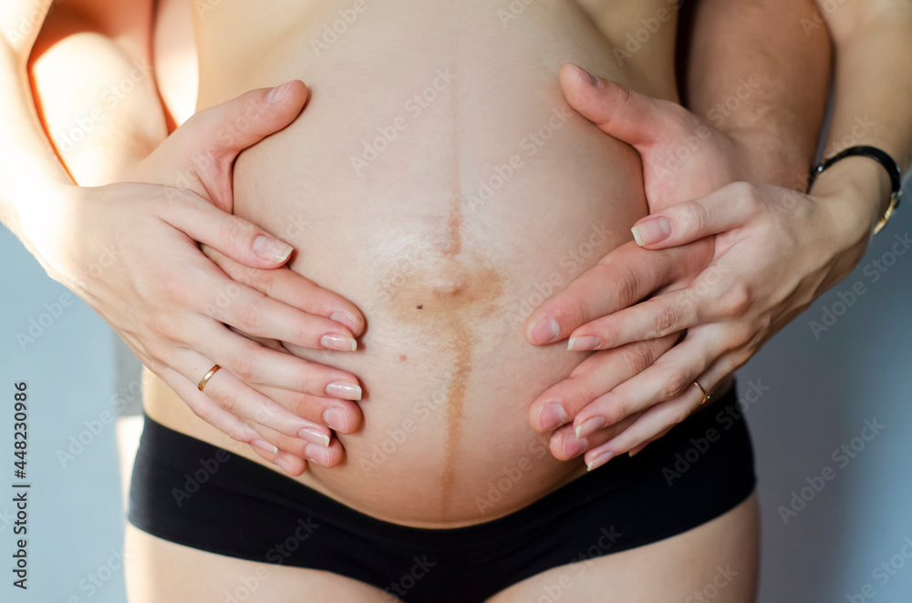 Male and female hands on a pregnant tummy