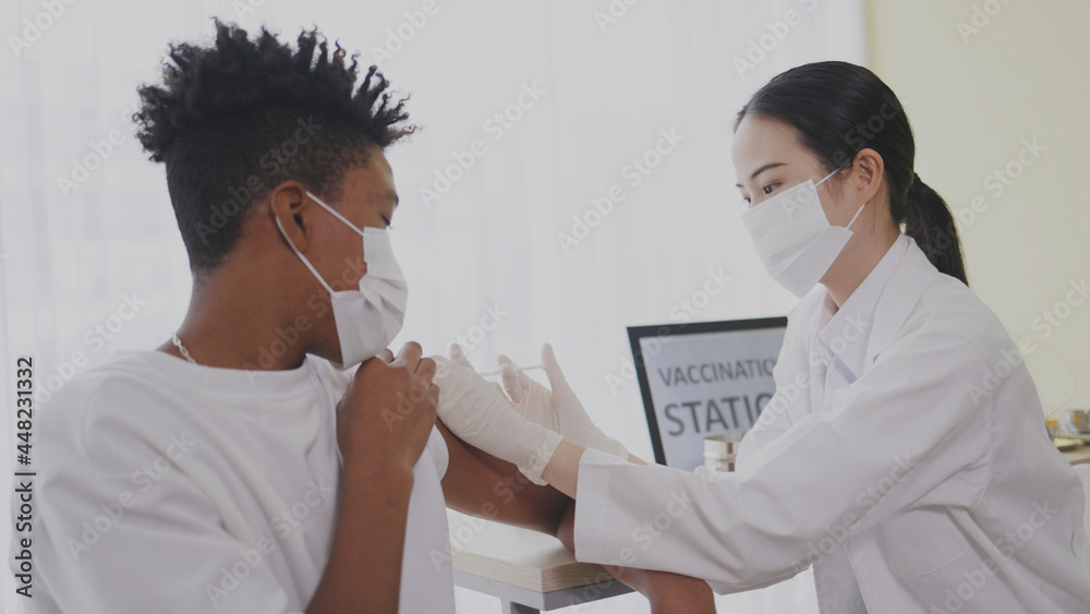 Obraz premium African American teenager wearing face mask sit in hospital waiting for COVID-19 vaccination. Epidemic Control with Inject at Clinic. Concept health care