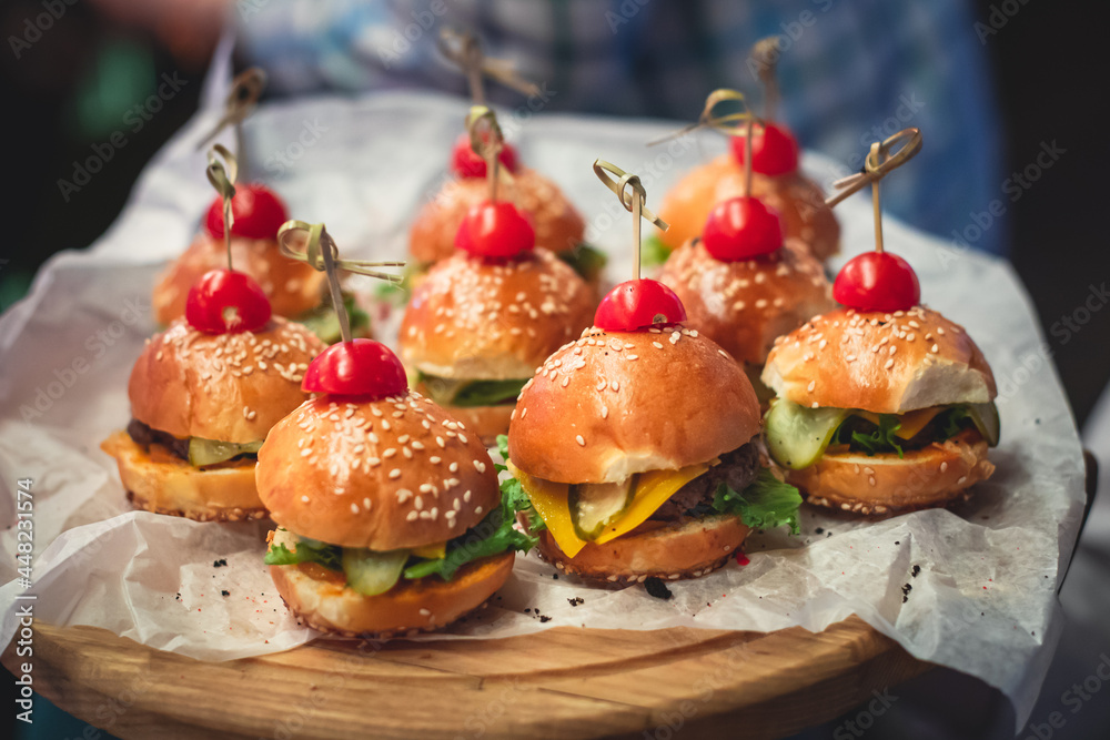 Burger mini burgers snacks on a wooden table with craft paper, beautifully decorated catering banquet table on corporate christmas birthday party event or wedding celebration - obrazy, fototapety, plakaty 