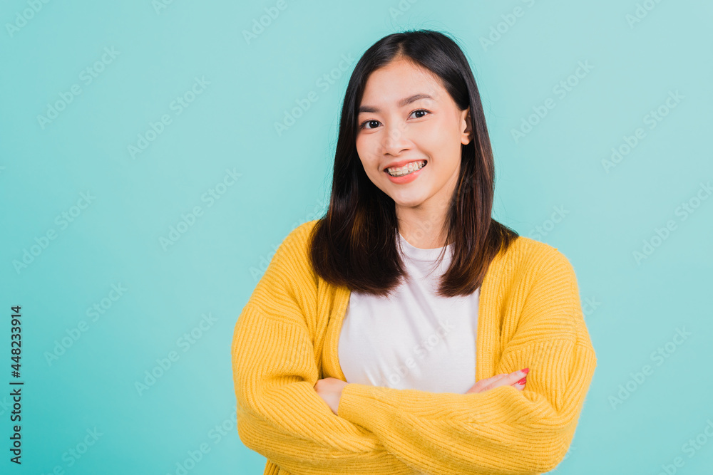 Fototapeta premium Young Asian beautiful woman smiling wear silicone orthodontic retainers on teeth with crossed arms, studio isolated on blue background, retaining tools after removable braces. Dental hygiene concept