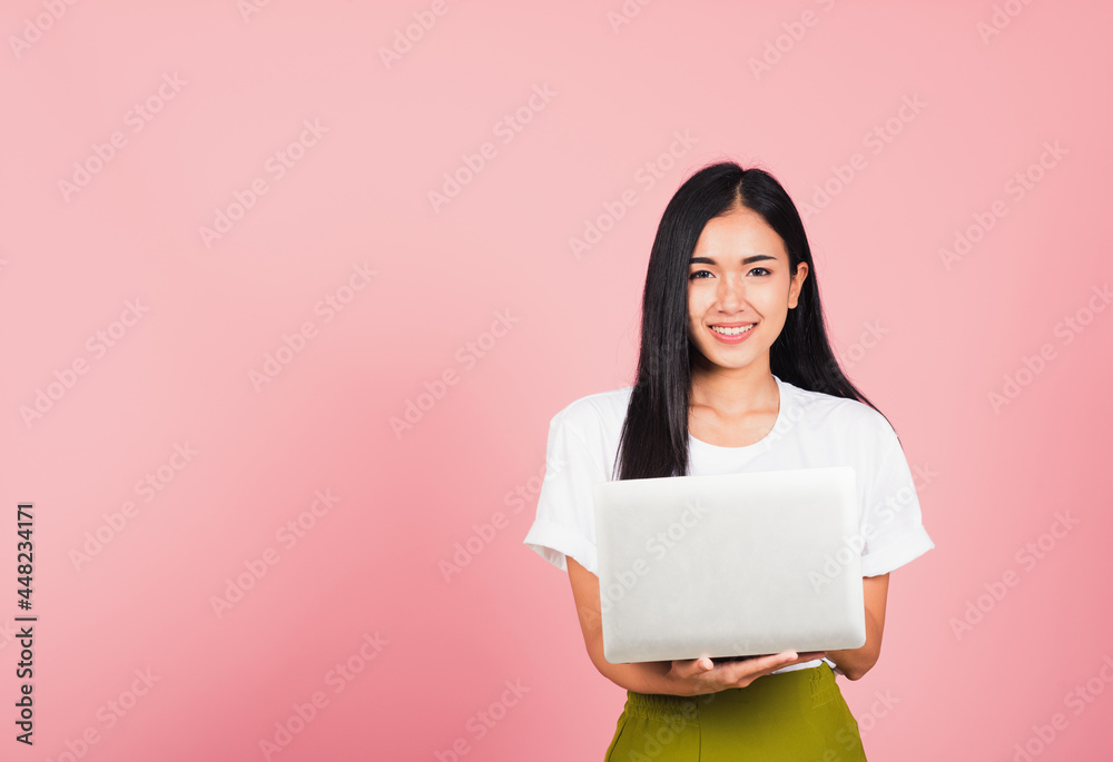 Portrait of happy Asian beautiful young woman confident smiling face holding using laptop computer looking to camera, studio shot isolated on pink background, with copy space Portrait of happy Asian beautiful young woman confident smiling face holding using laptop computer looking to camera, studio shot isolated on pink background, with copy space