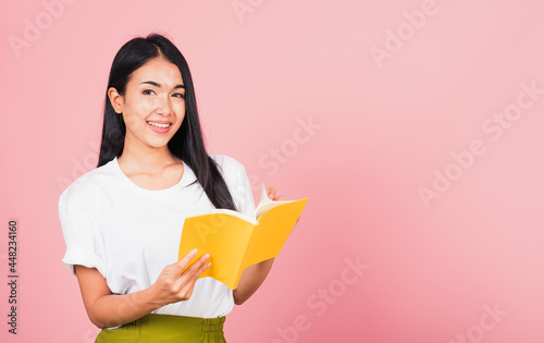 Portrait of beautiful Asian young woman teenage smiling holding a yellow book and reading, studio shot isolated on pink background with copy space