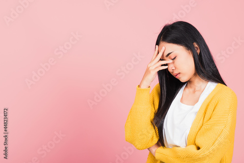 Portrait of beautiful Asian young woman sad tired strain face holding hold head by hands, female person closed eyes problem she headache, studio shot isolated on pink background photo