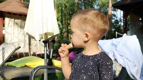 little cute adorable playful caucasian blond kid boy eating sweet tasty ice cream on hot summer day outdoors. Happy child enjoy dessert during vacation holiday at beach pool resort area outside