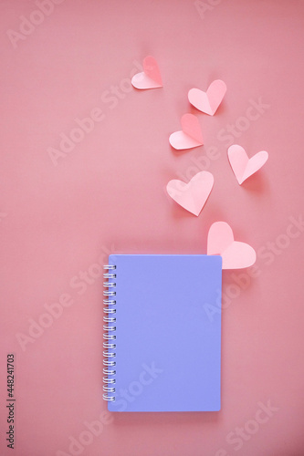 Purple notebook cover and cut out heart mockups on pink background. Symbol of love and Valentine's day. Flat lay, top view, copy space
