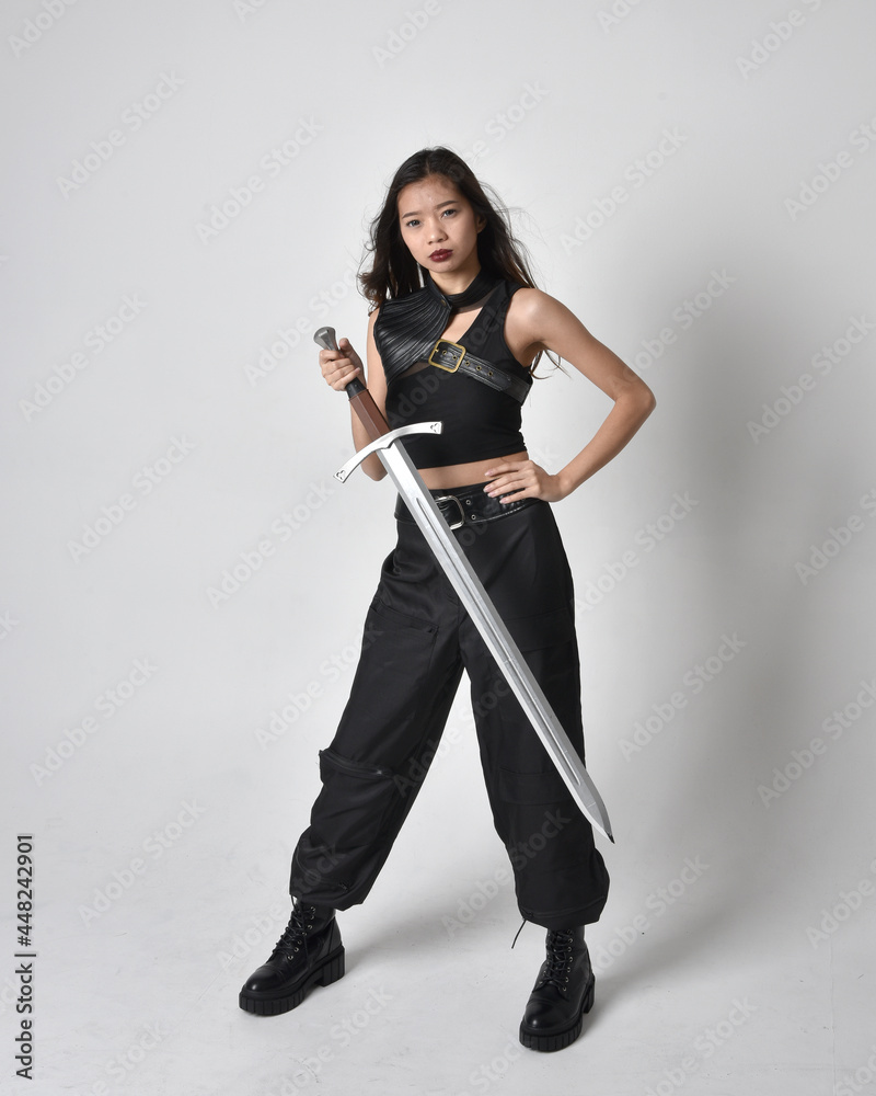 Full length portrait of pretty young asian girl wearing black tank top, utilitarian pants and leather boots. Standing pose holding a sword, isolated against a studio background.
Full length portrait of pretty young asian girl wearing black tank top, utilitarian pants and leather boots. Standing pose holding a sword, isolated against a studio background.