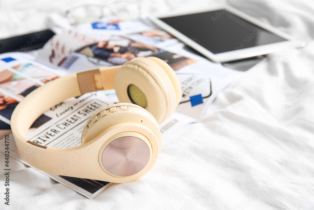 Modern headphones with magazine on bed, closeup Modern headphones with magazine on bed, closeup