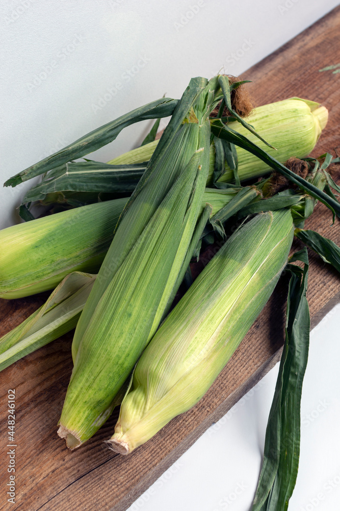 Fresh organic corn cobs unpeeled (in green leaves) on wooden board. Harvest concept. Local food. Fresh organic corn cobs unpeeled (in green leaves) on wooden board. Harvest concept. Local food.