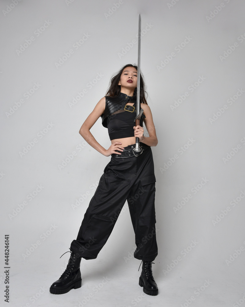 Full length portrait of pretty young asian girl wearing black tank top, utilitarian pants and leather boots. Standing pose holding a sword, isolated against a studio background.
Full length portrait of pretty young asian girl wearing black tank top, utilitarian pants and leather boots. Standing pose holding a sword, isolated against a studio background.