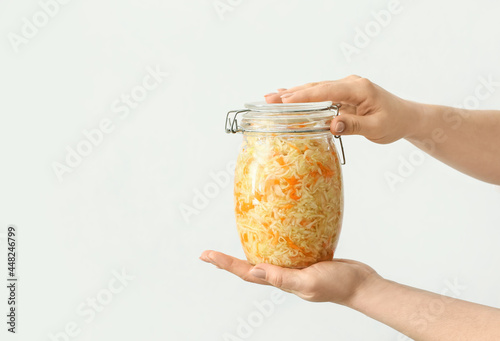 Woman with glass jar of tasty sauerkraut on light background, closeup