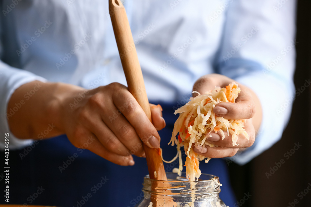 Woman putting tasty sauerkraut in glass jar on dark background, closeup Woman putting tasty sauerkraut in glass jar on dark background, closeup