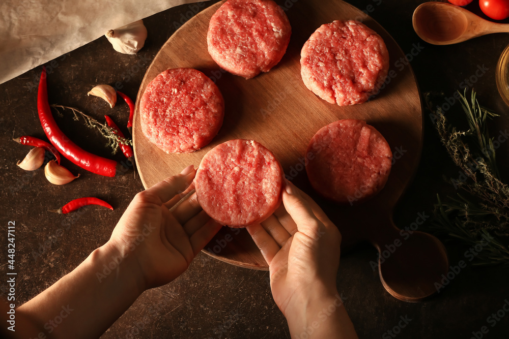 Woman preparing tasty cutlets made of fresh forcemeat on dark
