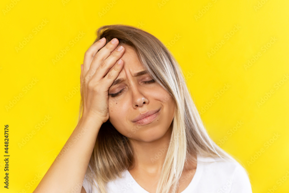 Headache pain. A young caucasian beautiful blonde woman with a head ache holding her forehead isolated on yellow background Headache pain. A young caucasian beautiful blonde woman with a head ache holding her forehead isolated on yellow background