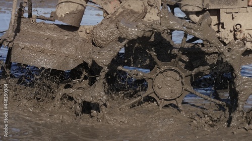 A close up of splashes of mud on a grouser of a tilling machine. A plougher equipment on a farm. Taming soil before seeding. RIce field agricultural industry. Spring labour. photo