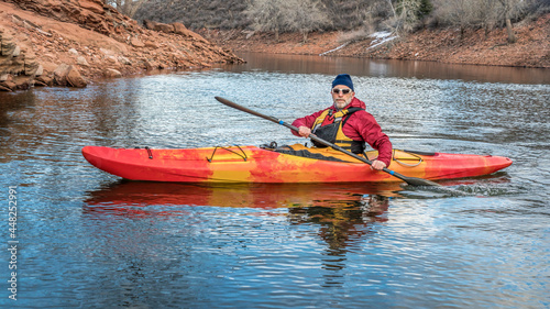 senior male paddler is paddling colorful river kayak on a calm lake - recreation concept, cold season on Horsetooth Reservoir in Colorado