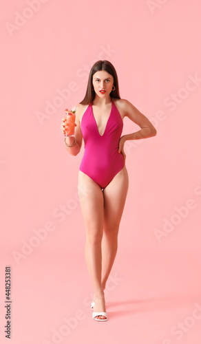 Beautiful young woman in swimsuit and with cocktail on color background