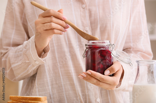 Woman holding jar with tasty cherry jam in kitchen, closeup