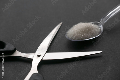 Scissors and a white sugar in a transparent spoon on black background. photo