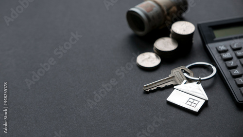 House key together with calculator, money and a stack of coins on black background.