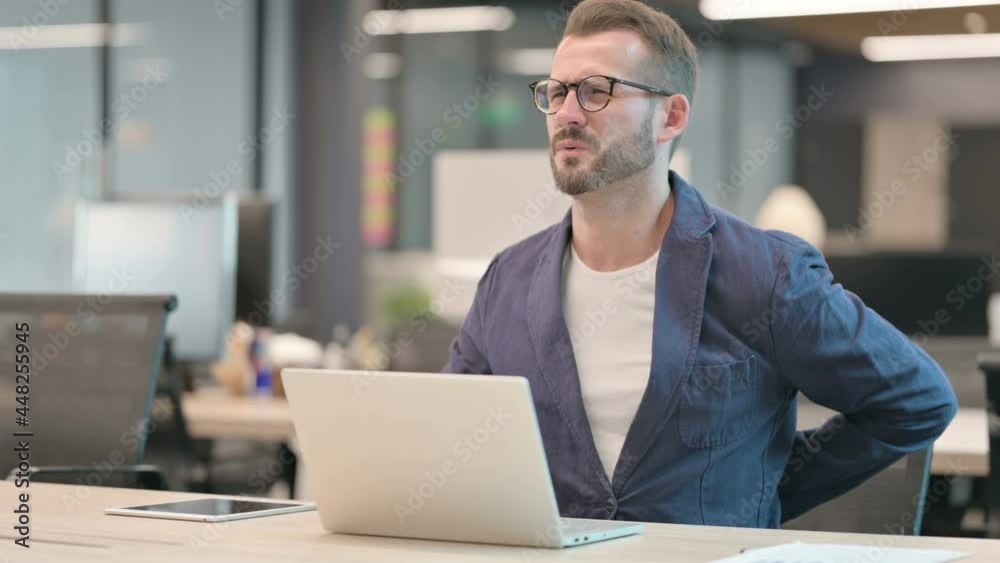 Middle Aged Businessman having Back Pain while using Laptop in Office Middle Aged Businessman having Back Pain while using Laptop in Office