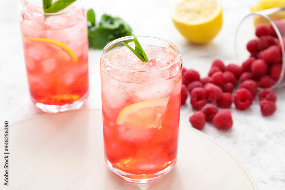 Glasses with tasty raspberry lemonade on light background