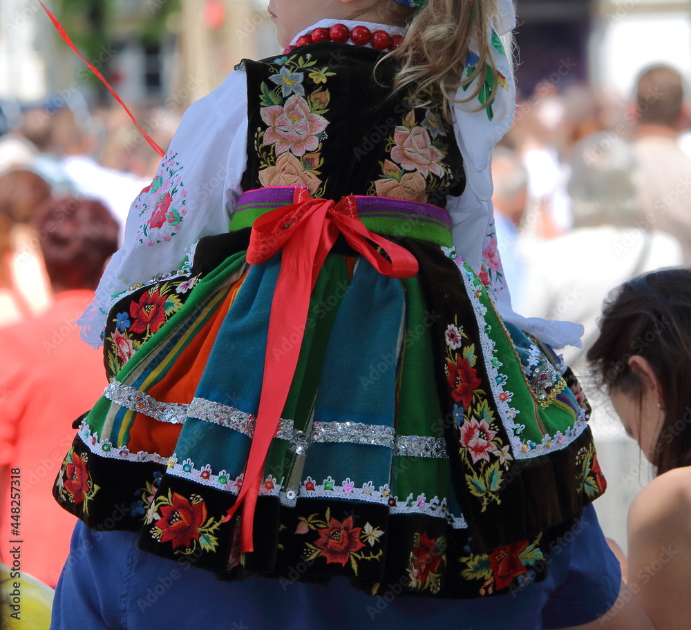 Girl child in traditional folk costume from Lowicz region in Poland on her fathers back while join Corpus Christi procession