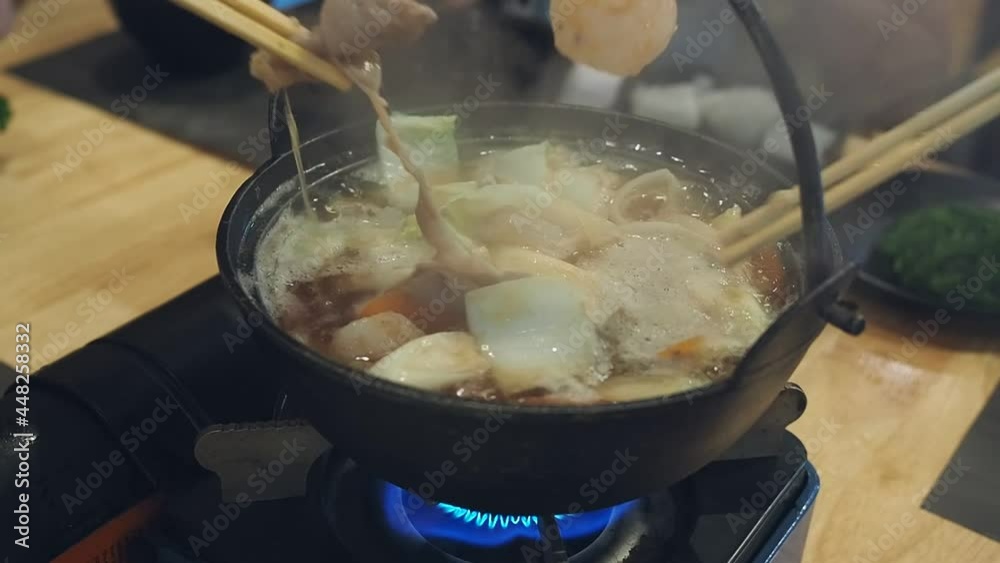 Each members of the dining table used chopsticks to grab food (pork, beef, vegetables, seafood) from a Shabu Shabu pot in a japanese restaurant. Shabu-shabu meal with family. Each members of the dining table used chopsticks to grab food (pork, beef, vegetables, seafood) from a Shabu Shabu pot in a japanese restaurant. Shabu-shabu meal with family.