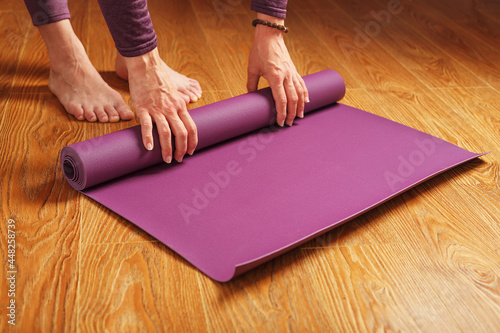 A girl folds a lilac yoga mat after a practice workout on a wooden floor
