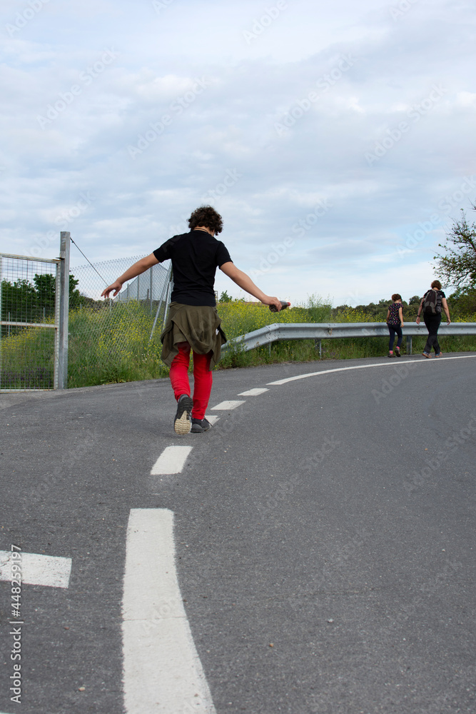 Curly-haired teenager balancing on road shoulder markings.