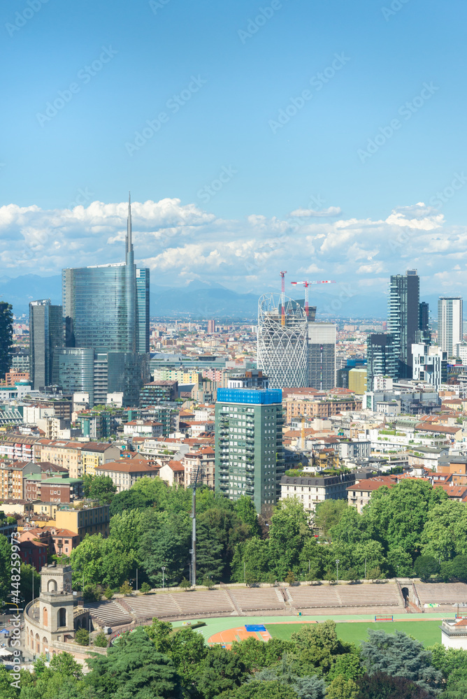 Vertical aerial view of Milan skyline, Italy, with business skyscrapers. In the distance the alps mountain range is visible. Blue sky and white clouds on the background.