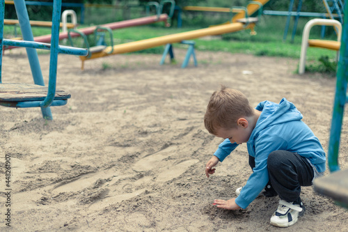 Little boy plays with sand on the playground © Klochkov