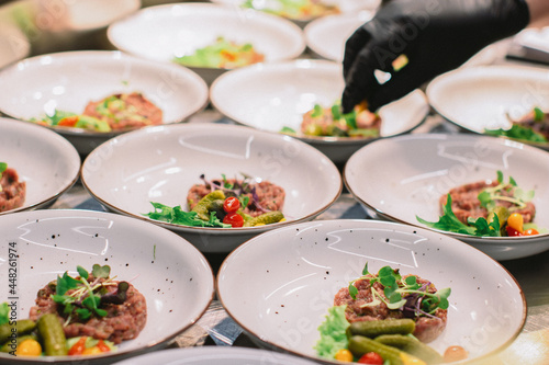 chef is serving fresh beef tartar with quail eggs, marinated and fresh vegetables on rucola on the white plates before the party