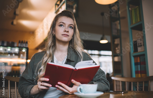 Pensive woman sitting with book in cafeteria