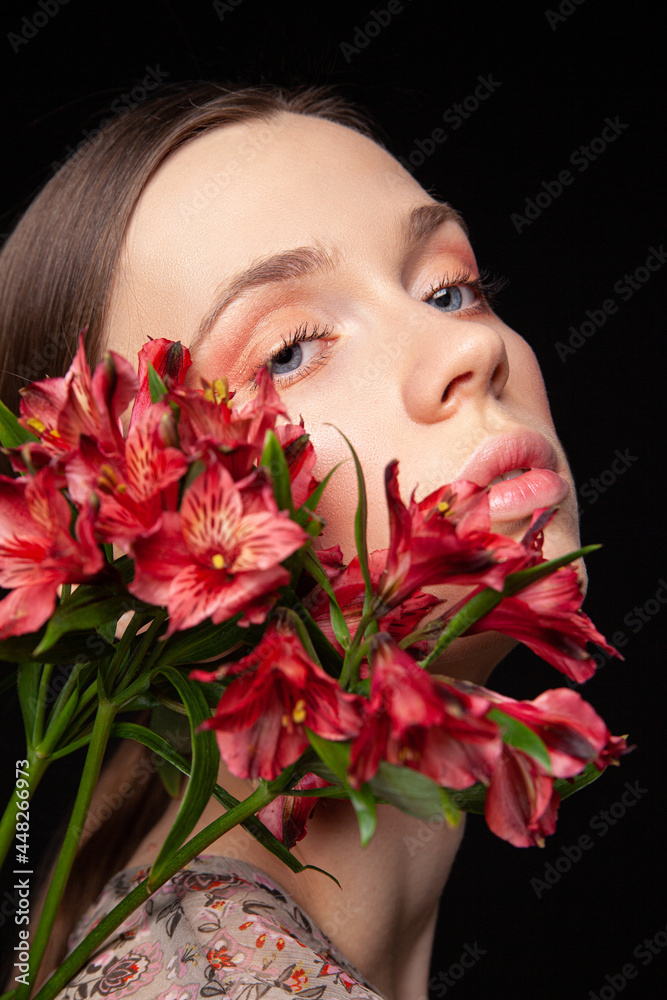 Side view of young female model enjoying softness of delicate red flowers on black background Side view of young female model enjoying softness of delicate red flowers on black background