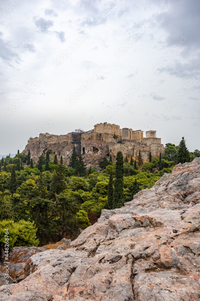 Acropolis (Parthenon, Propylaea, Temple of Athena Nike, Hekatompedon Temple) in summer greenery, Athens ancient historical landmark in city center with rocky Areopagus - Hill on cloudy day. Vertical