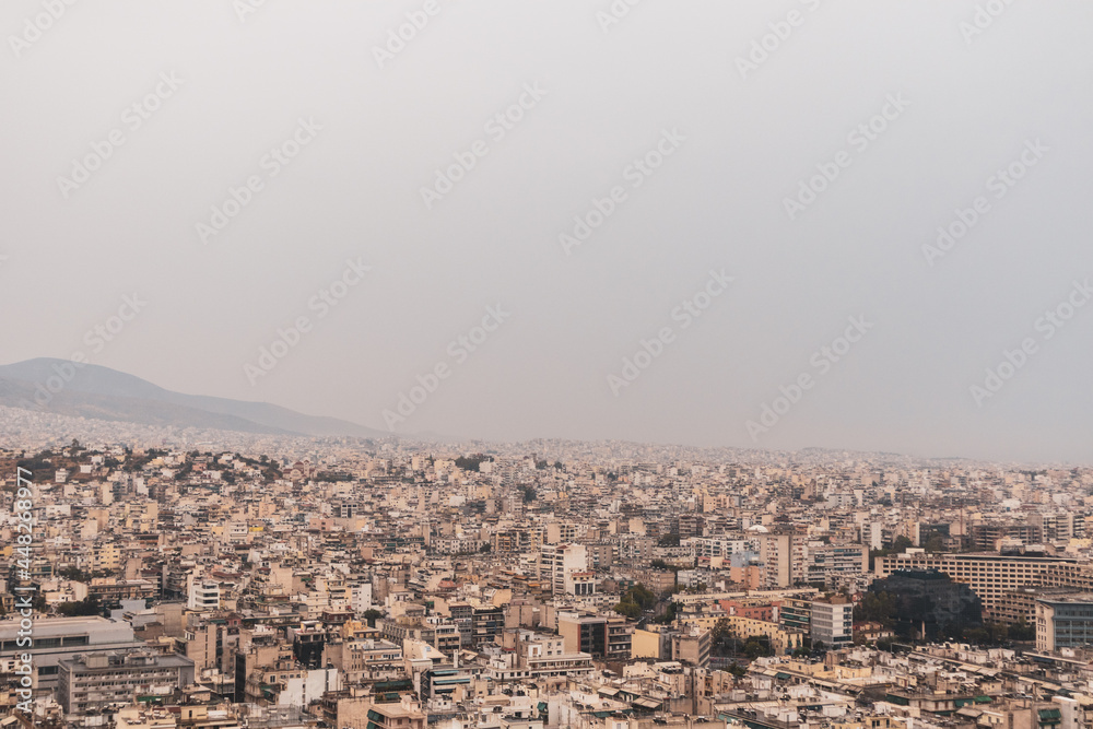 Athens city center overcrowded streets with white buildings architecture on cloudy foggy day. Rooftop view from Filopappou Hill near Acropolis, Greece. Warm colors