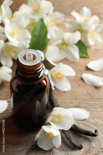 Jasmine essential oil and fresh flowers on wooden table
