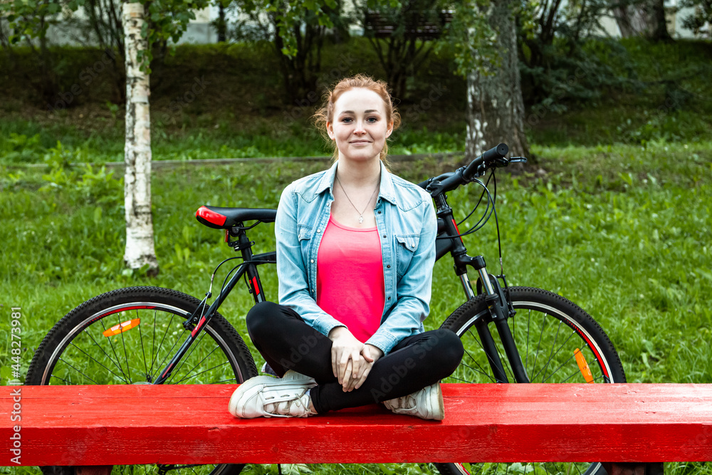 Obraz premium A cheerful girl with a bicycle sits on a park bench.