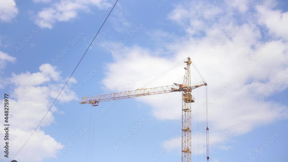 The work of a yellow construction crane. Building on blue sky cloudy background. Heavy construction machinery. Rule of Thirds. Minimalistic HD horizontal video. time laps, accelerated shooting