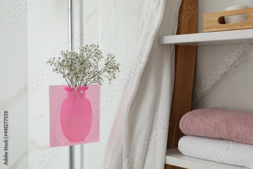 Silicone vase with flowers on shower glass panel in bathroom